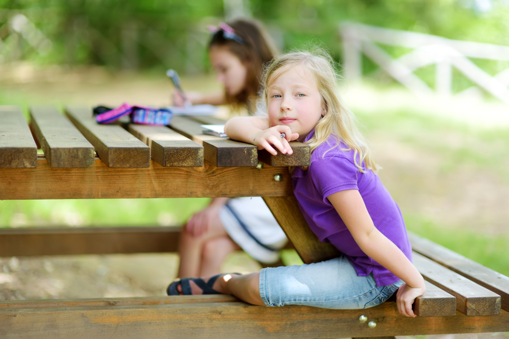 Two happy sisters drawing together at the wooden table outdoors